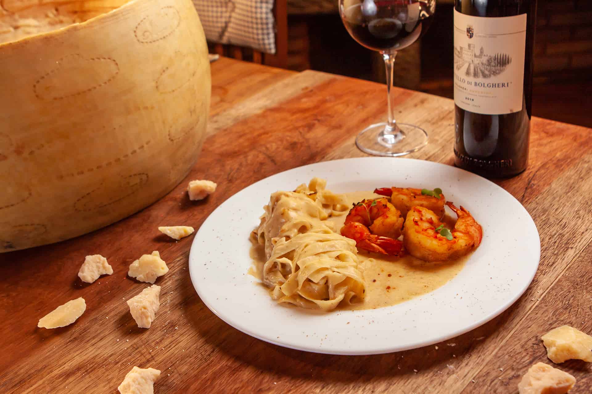 Massa com camarões ao lado de uma roda de parmesão